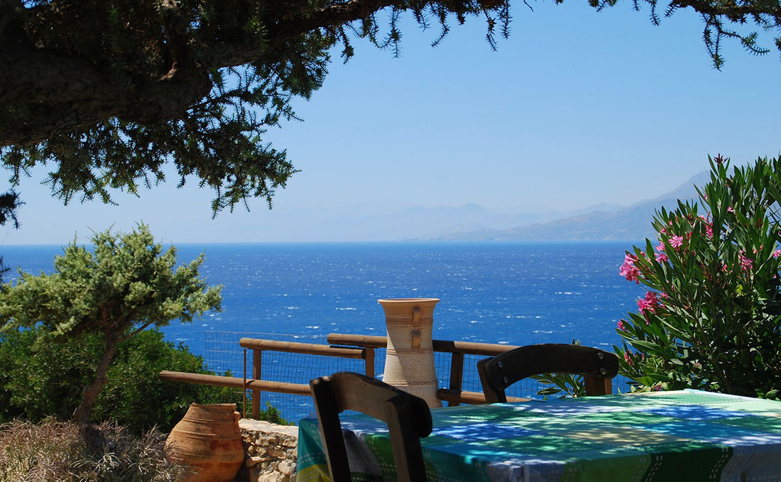 Blick von einer schattigen Terrasse auf das Meer mit Bergen im Hintergrund, Griechenland